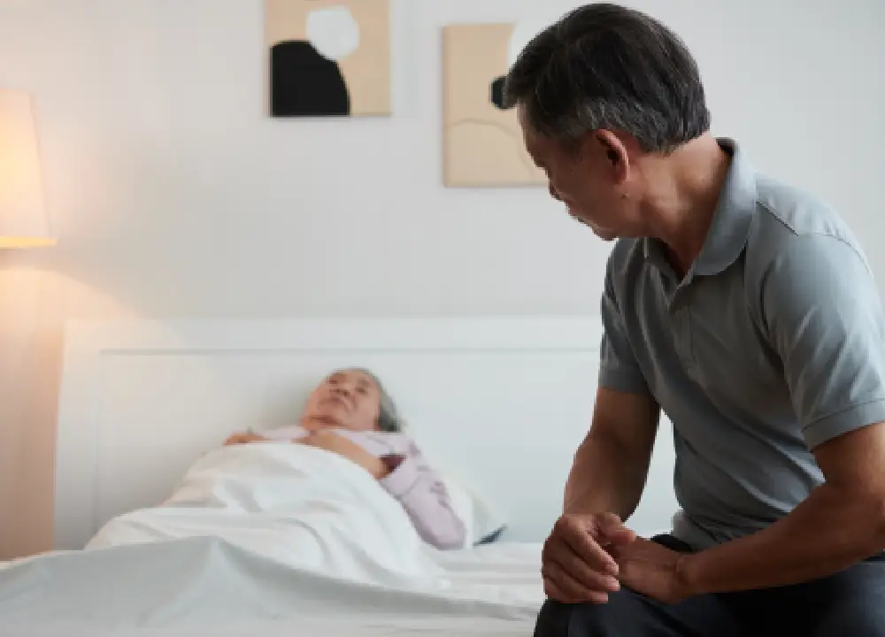 Man sitting beside his wife resting in bed, showing calm emotional support after a serious diagnosis