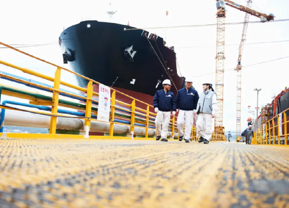Shipyard workers walking along a dock near large vessels and cranes, representing maritime occupations at high risk for asbestos exposure.